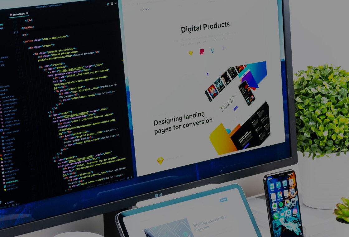 A desktop monitor showing a code editor beside the web page it renders, with a tablet, phone and coffee cup on the desk